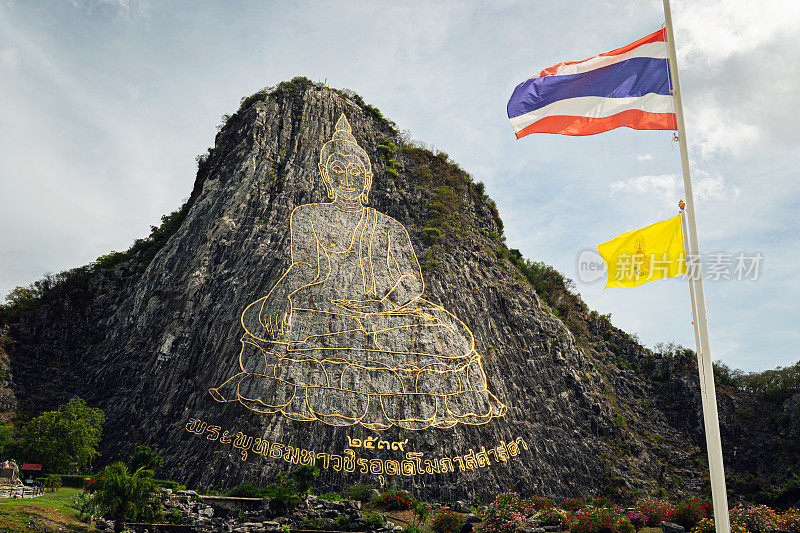 泰国全武里佛山Khao Chi Chan Sattahip区。芭堤雅附近的宗教景点。岩石上的金色佛像和多云天空背景上的泰国国旗